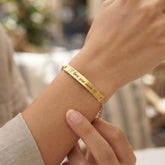 A close-up of a gold bracelet worn on a person's wrist, featuring engraved text that reads 'I love you always' with a small heart, and a delicate chain extension.