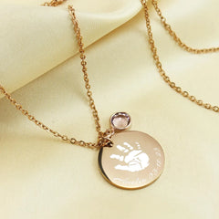 "Custom baby handprint necklace in silver—a perfect new mom gift or push present. This keepsake jewelry features an actual handprint engraving and a birthstone accent, shown styled on a person."