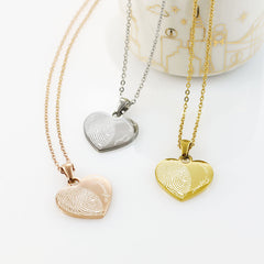 "Three custom heart-shaped fingerprint necklaces in rose gold, silver, and yellow gold. Each pendant features a detailed half-heart fingerprint engraving paired with personalized names like 'Grandpa,' 'Love Dad,' and 'Love Papa' in an elegant script font."
