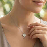 Woman wearing a silver heart-shaped necklace with a blurred natural background