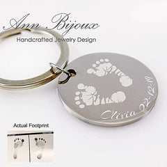 Personalized silver disc keychain featuring an engraving of a baby's actual footprints, the name "Olivia," and a date. A custom commemorative new parent gift or memorial keepsake.