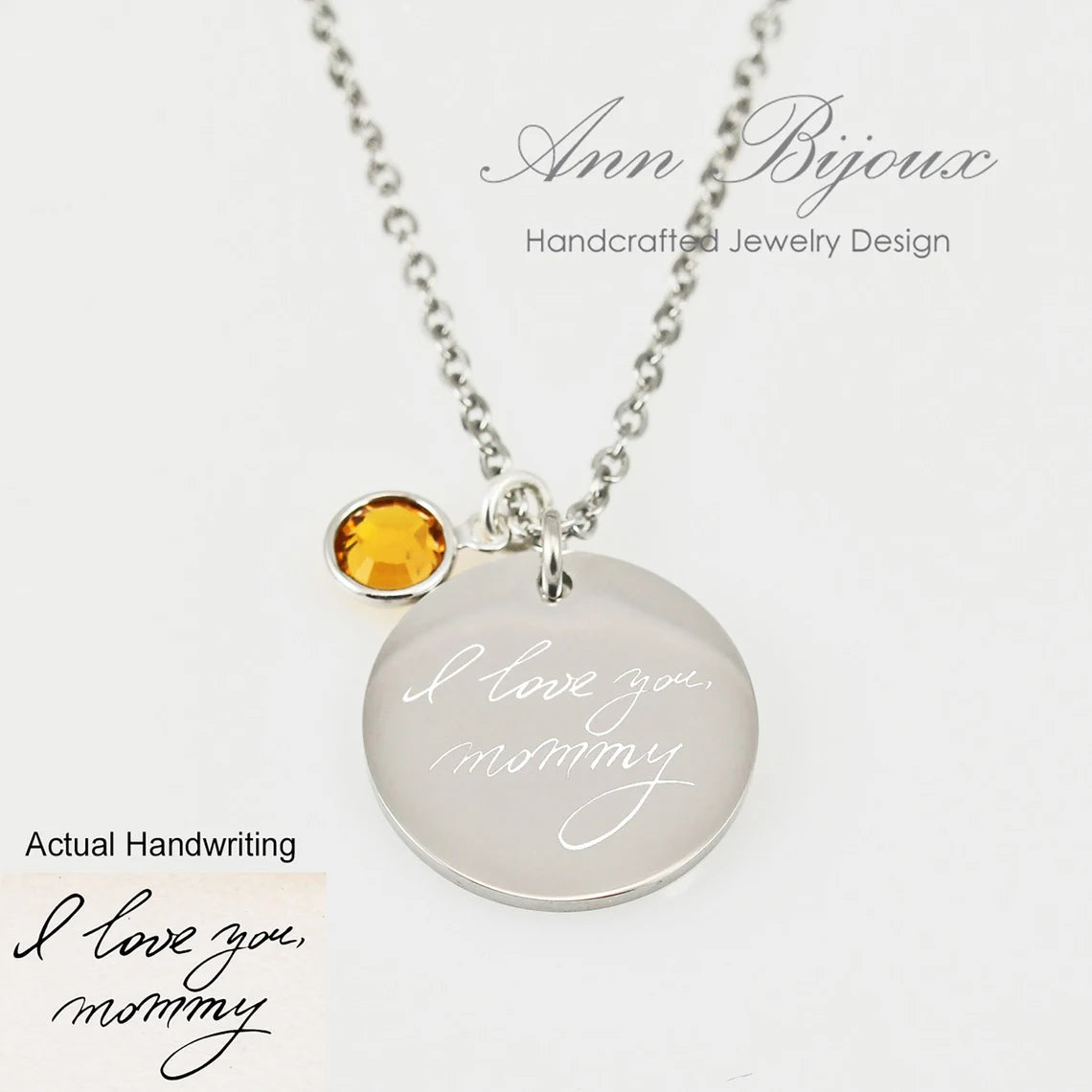 "The pendant includes a name and date etched along the bottom edge, paired with a small amber-colored birthstone charm on a delicate chain."