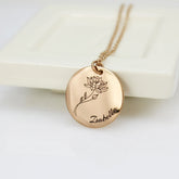 A stainless steel necklace with a round pendant featuring a laser engraved birth flower and the name 'Zabella' on it.