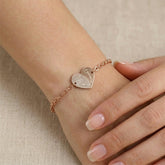 Rose gold bracelet with a heart-shaped charm on a wrist against a beige background