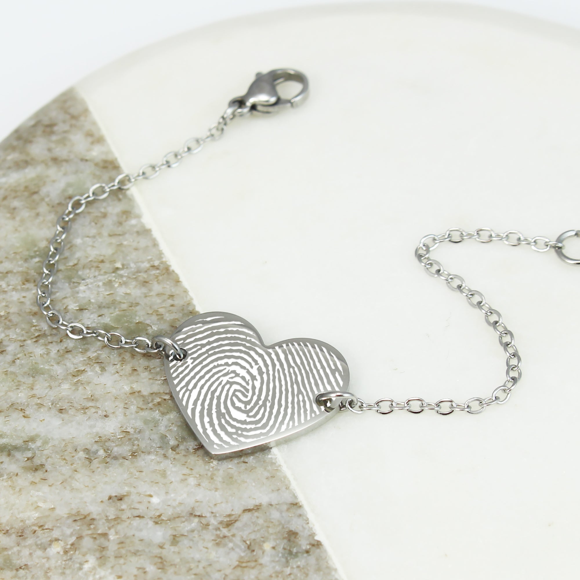 Silver bracelet with a heart-shaped fingerprint charm on a stone surface