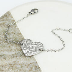 Silver bracelet with a heart-shaped fingerprint charm on a stone surface