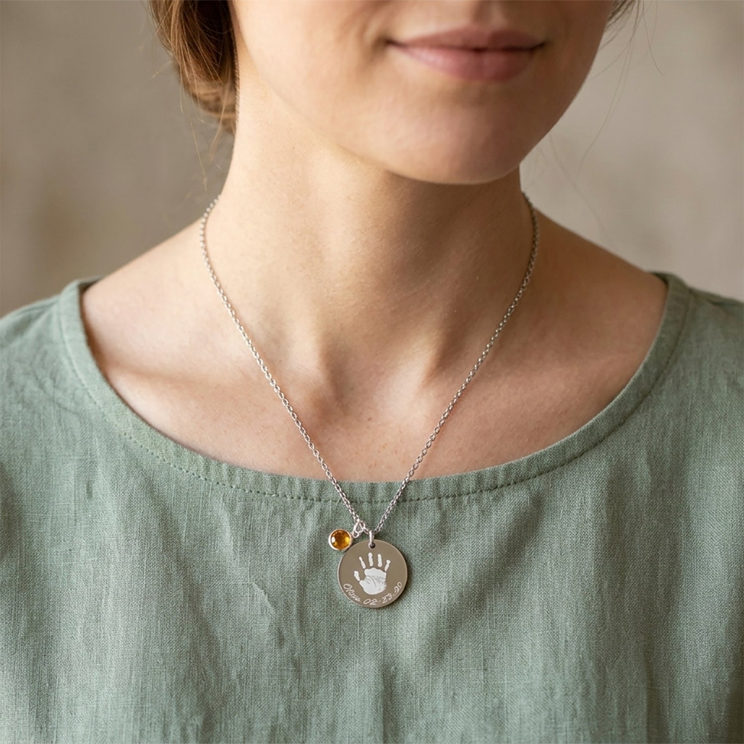 Person wearing a necklace with a handprint pendant on a neutral background