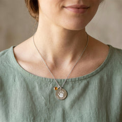 Person wearing a necklace with a handprint pendant on a neutral background
