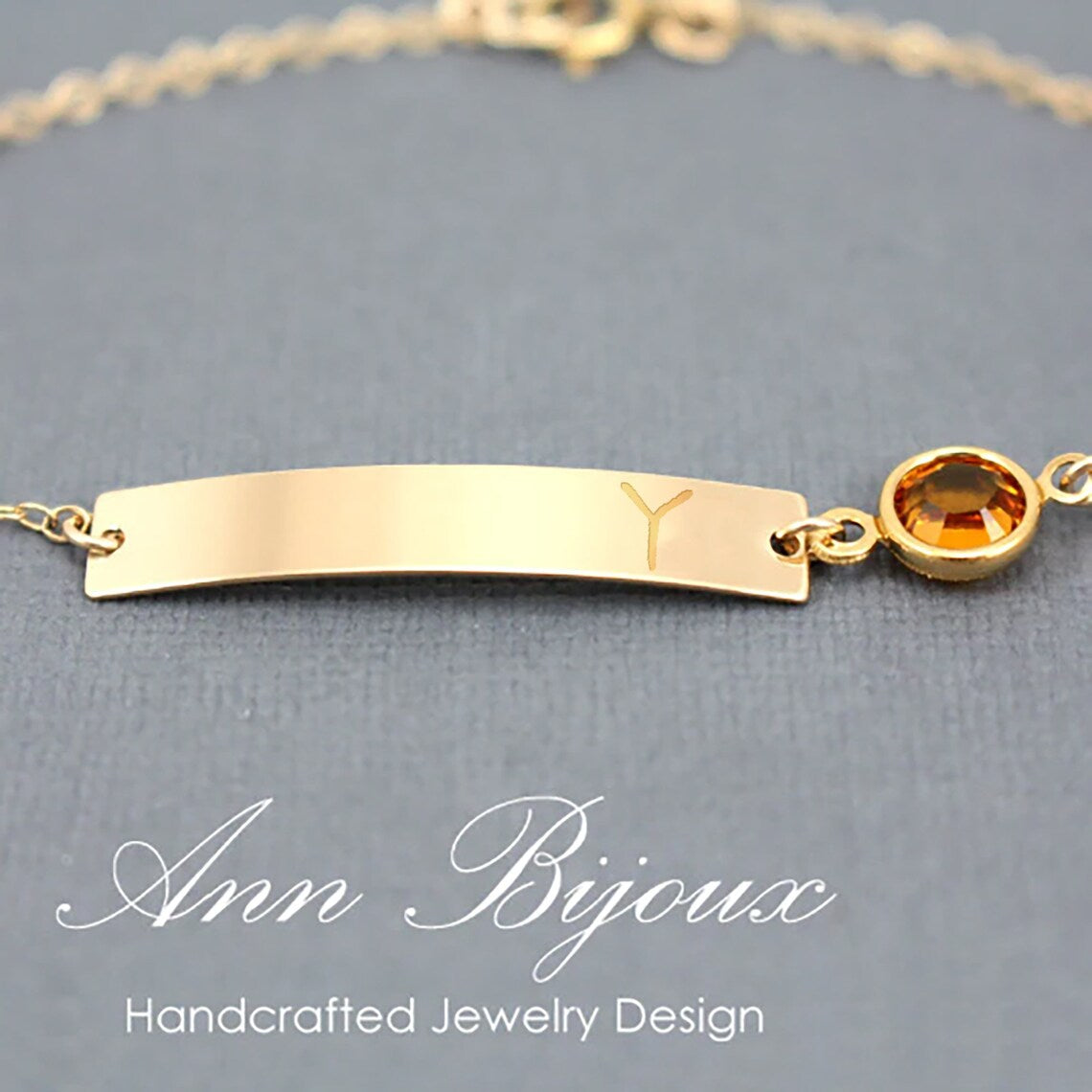 Personalized gold bar bracelet featuring an engraved initial "Y" and a round amber birthstone charm on a delicate gold chain. A custom nameplate jewelry piece for women or as a bridesmaid gift.