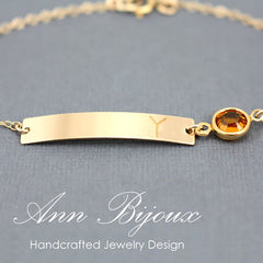 Personalized gold bar bracelet featuring an engraved initial "Y" and a round amber birthstone charm on a delicate gold chain. A custom nameplate jewelry piece for women or as a bridesmaid gift.