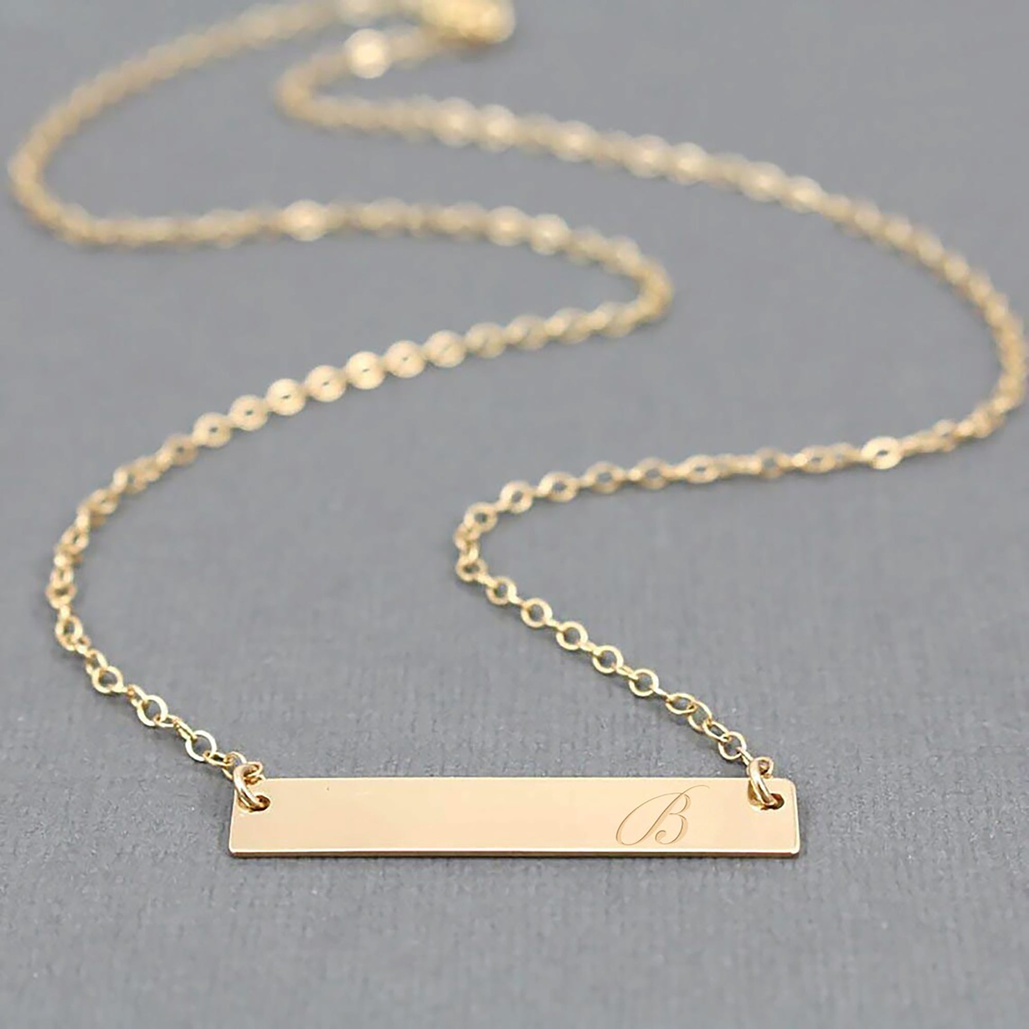 Gold bar necklace with engraved letter 'B' on a gray background