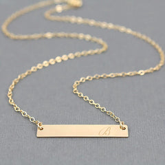 Gold bar necklace with engraved letter 'B' on a gray background