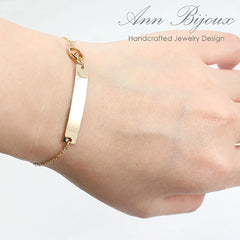 Gold initial bar bracelet with a small orange gemstone accent. Custom engraved nameplate bracelet on a thin gold link chain, perfect for stacking or personalized gifting.