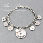 A bracelet with laser engraved stainless steel discs with the letters 'G', 'R', 'A', 'M', 'A' and an engraved heart that reads 'GRANDMA', attached to a stainless steel cable chain with a fresh water pearl.