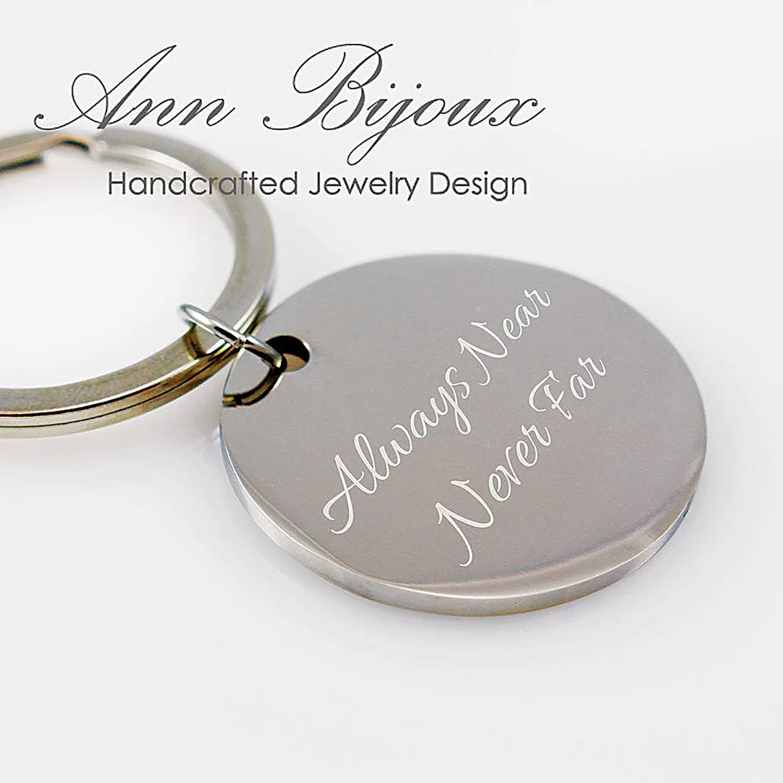 A round silver pendant attached to a keyring, engraved with a pair of tiny infant footprints, the name "Olivia" in script, and the date "02-12-19." A small inset image shows the original ink footprints used for the engraving.