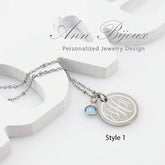 A stainless steel engraved monogram pendant necklace with a birthstone accent, displayed on a white background with the brand name 'Ann Bijoux'.