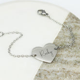 Silver bracelet with a heart-shaped tag engraved with 'Rocky' on a stone surface