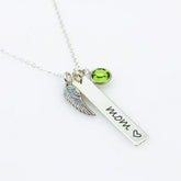 A sterling silver bar necklace with a wing charm and a green Swarovski crystal birthstone, engraved with the word 'Mom' and a heart symbol.