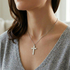 Person wearing a silver cross necklace with a neutral background