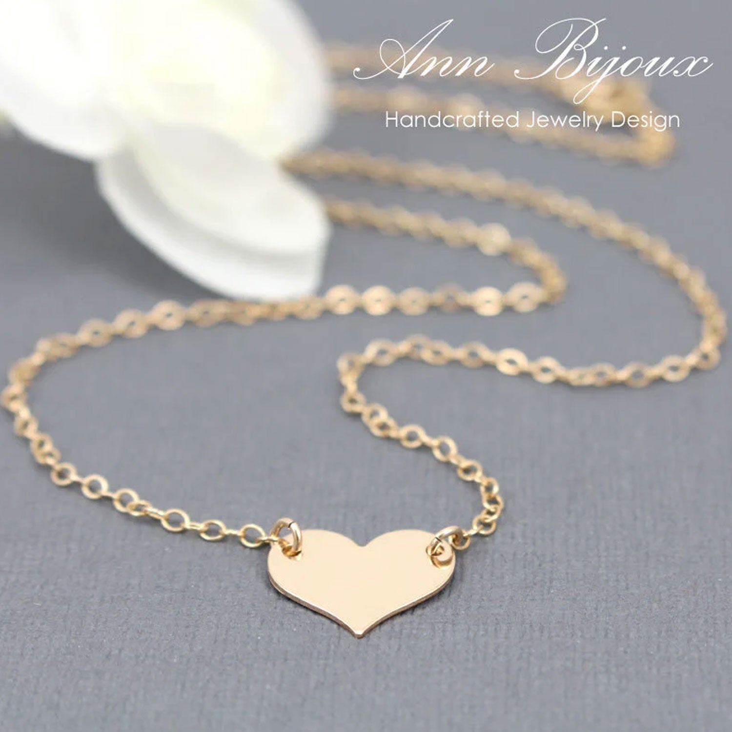 Gold heart-shaped pendant necklace on a gray surface with 'Ann Bijoux' branding.
