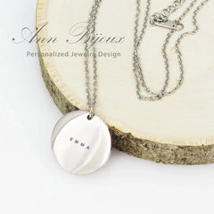 Three polished circular pendants in various metal finishes hanging from delicate cable chains, featuring custom name engravings and a small heart symbol.