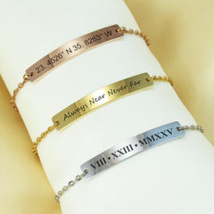 Three personalized bar bracelets in rose gold, yellow gold, and silver, displayed on a white fabric wrist form against a soft beige background. The bracelets feature engraved text including coordinates, a phrase, and Roman numerals.