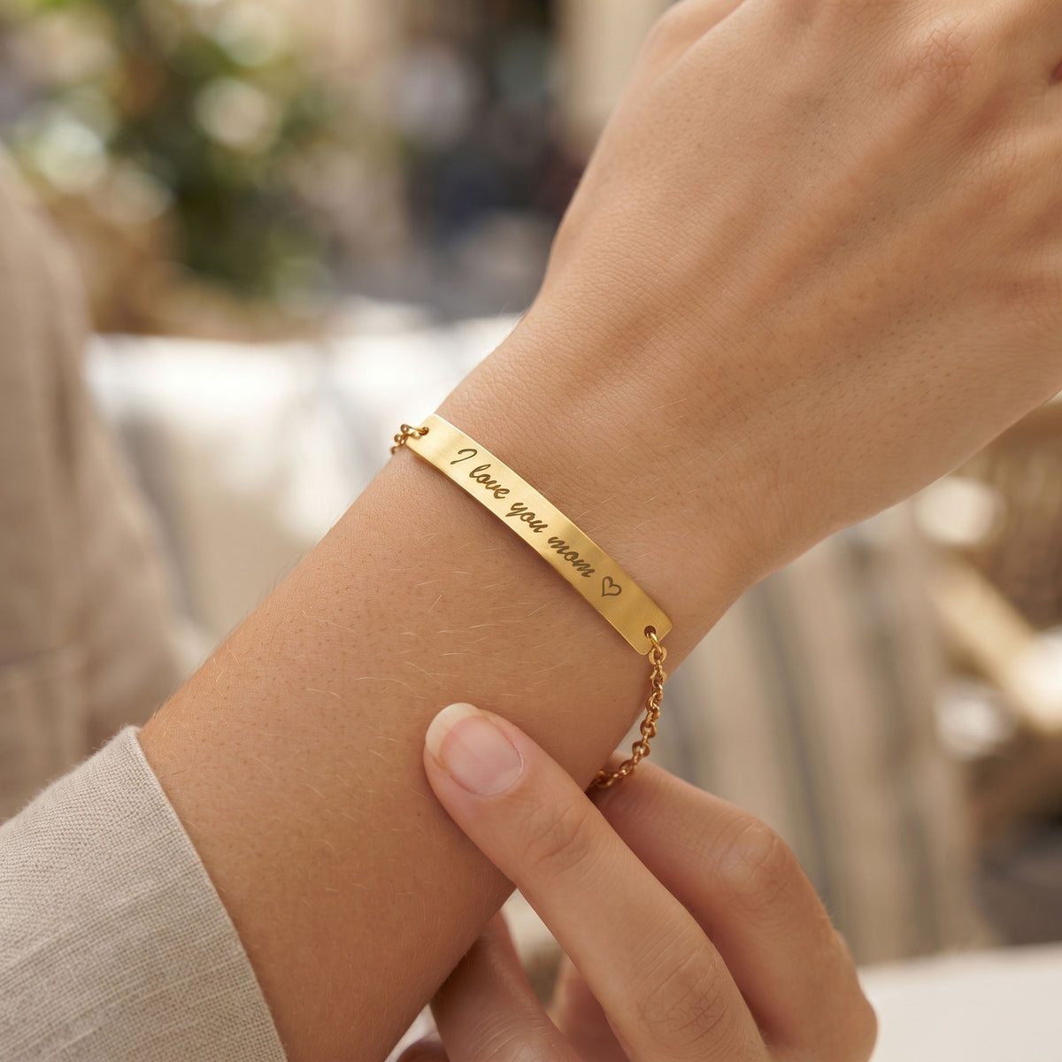 A close-up of a gold bracelet worn on a person's wrist, featuring engraved text that reads 'I love you always' with a small heart, and a delicate chain extension.