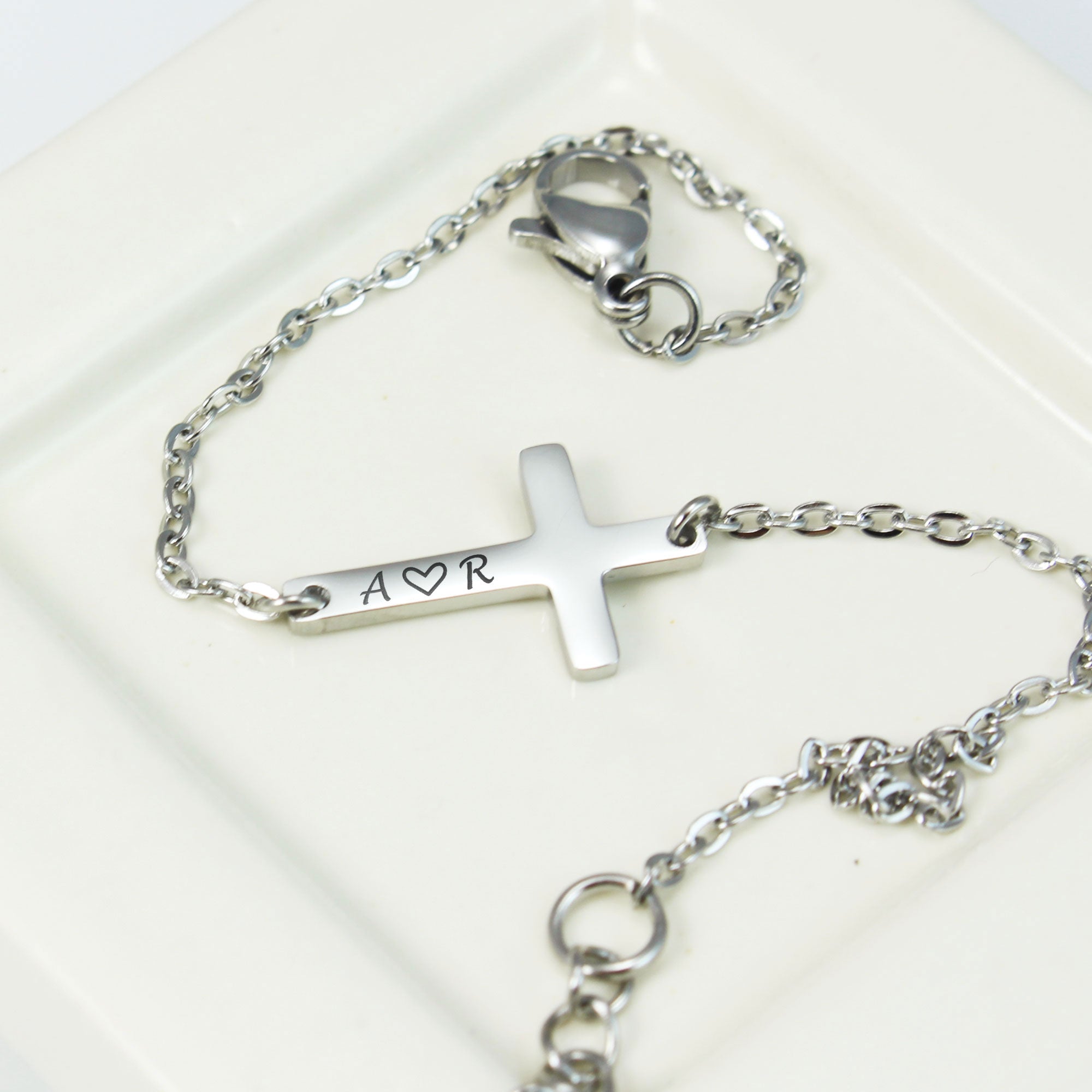 Silver bracelet with a cross charm and engraved letter on a white background