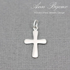 A polished silver cross pendant with a smooth, flat surface and a small top loop, displayed on a textured gray background with 'Ann Bijoux Handcrafted Jewelry Design' written in white script at the top.
