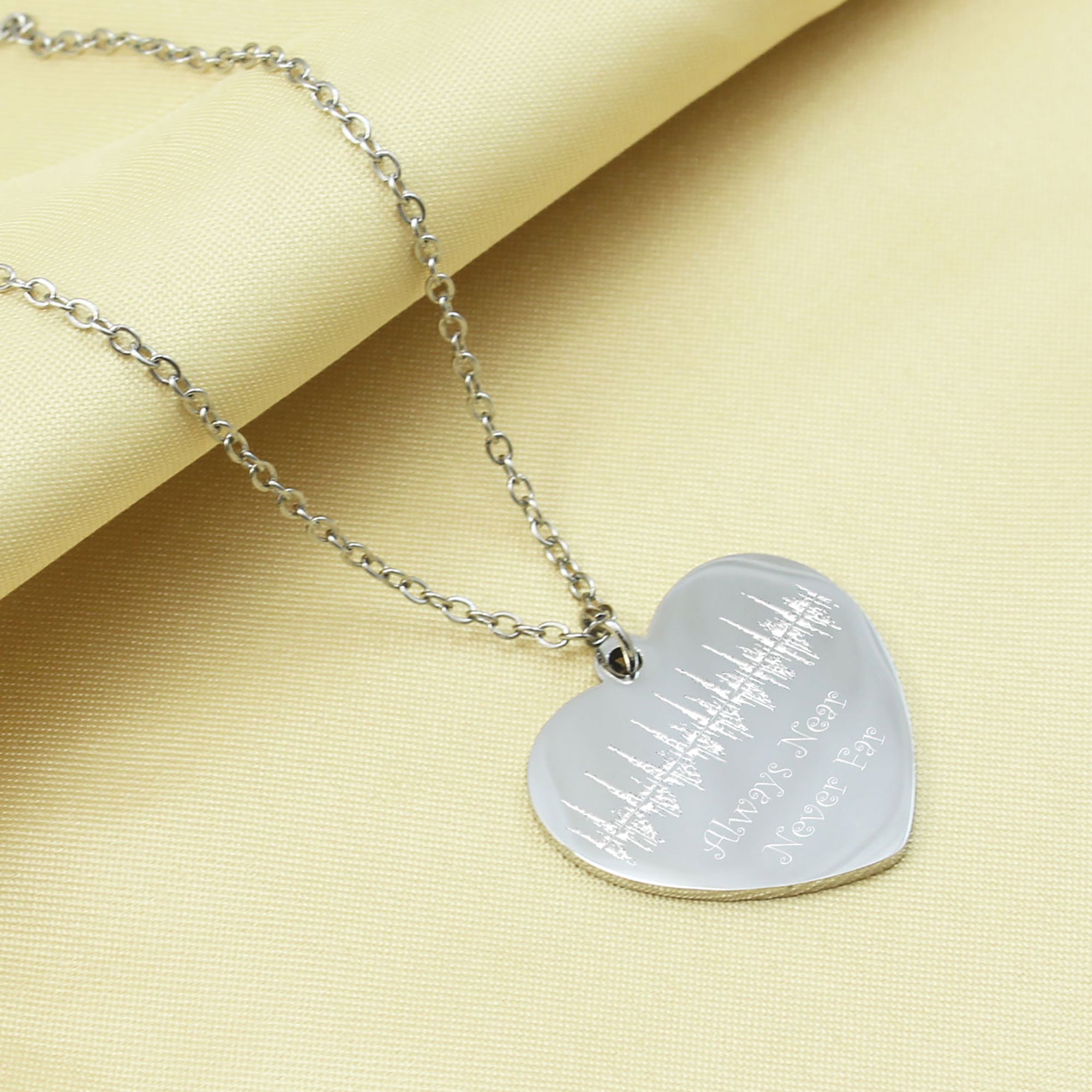Heart-shaped silver pendant necklace on a yellow fabric background