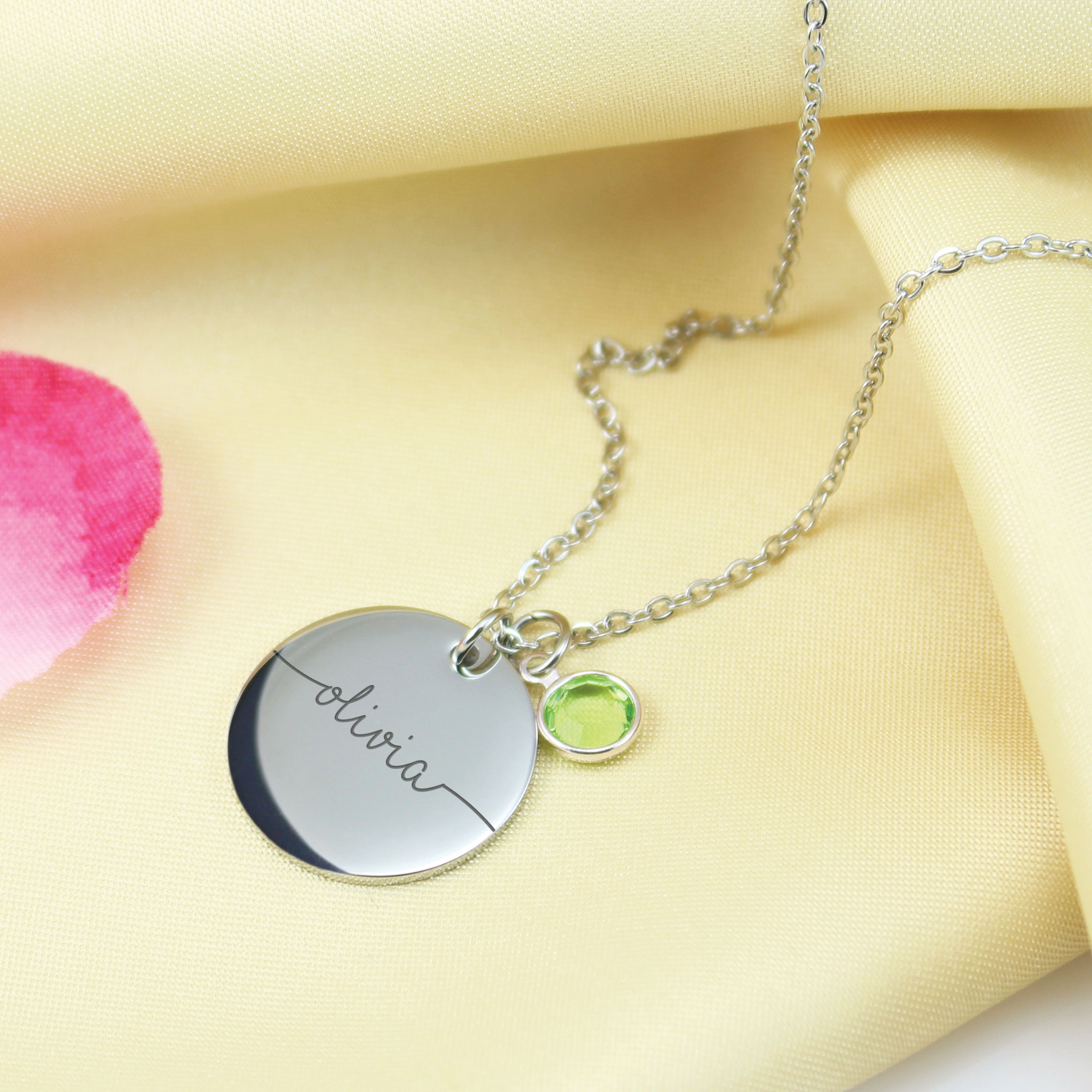 "Custom engraved name necklaces with round pendant discs and birthstone accents. Shown in three metal tones with cursive names and green, light blue, and pink crystals."