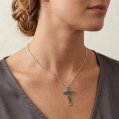 Silver cross necklace worn by a person with a neutral background