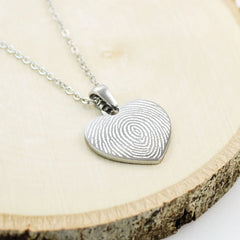 Personalized heart pendants engraved with unique fingerprints, shown in a trio of polished yellow gold, sterling silver, and rose gold.