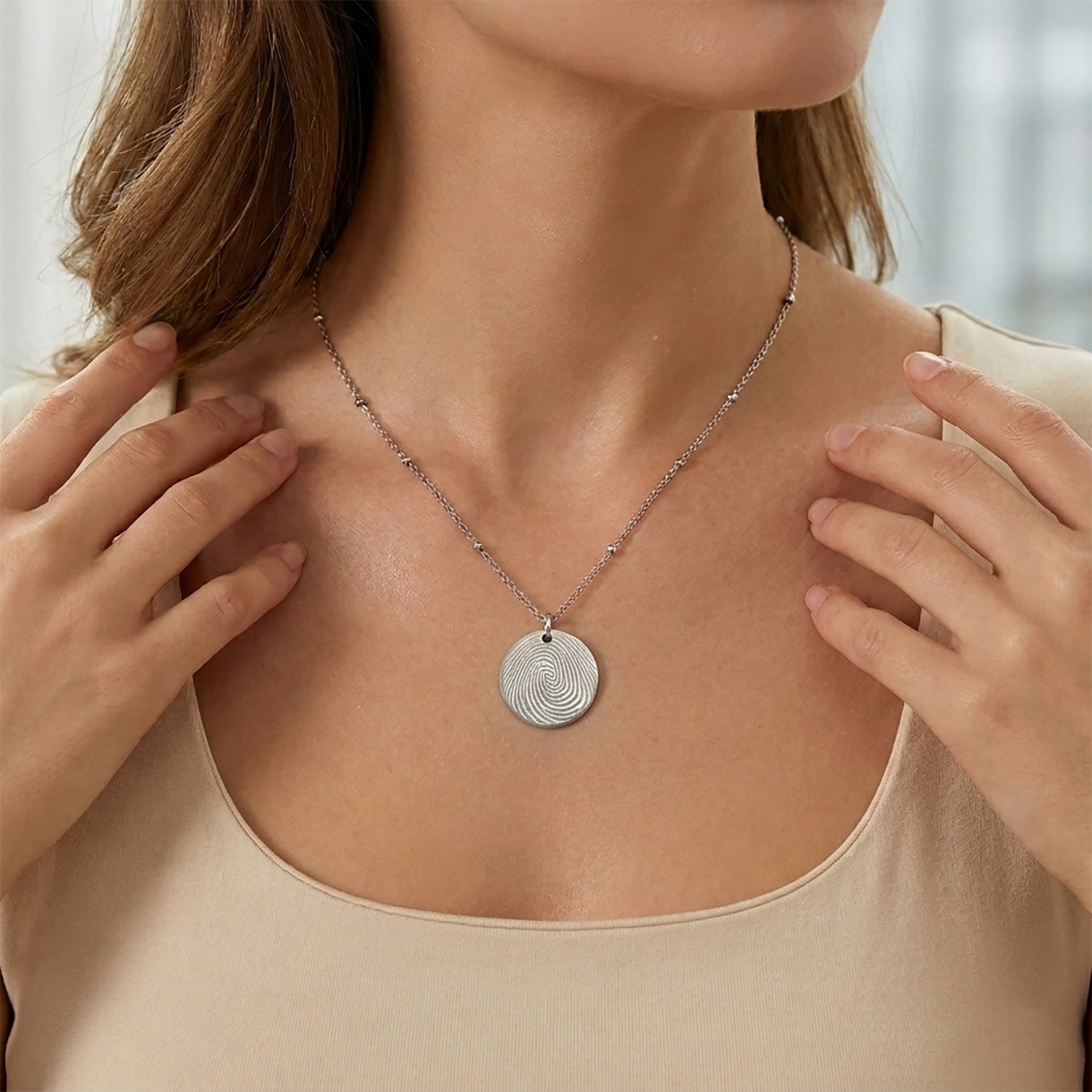 "Model wearing a personalized silver round disc necklace with a custom fingerprint engraving. The pendant hangs from a delicate satellite chain featuring small bead accents, shown on a person for scale."