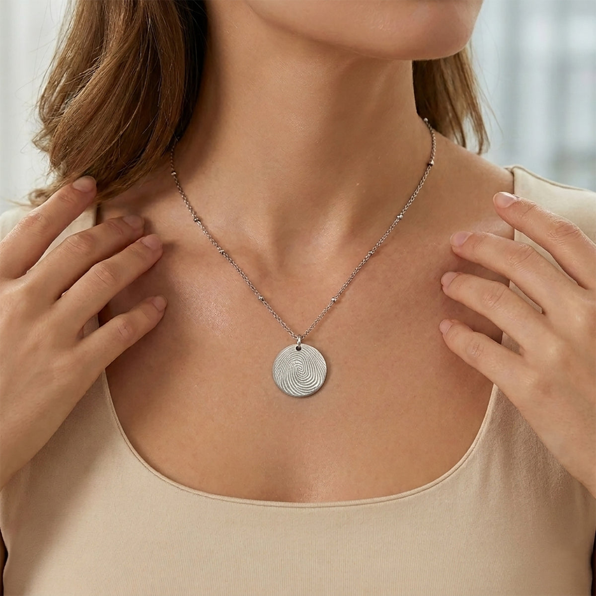 "Model wearing a personalized silver round disc necklace with a custom fingerprint engraving. The pendant hangs from a delicate satellite chain featuring small bead accents, shown on a person for scale."