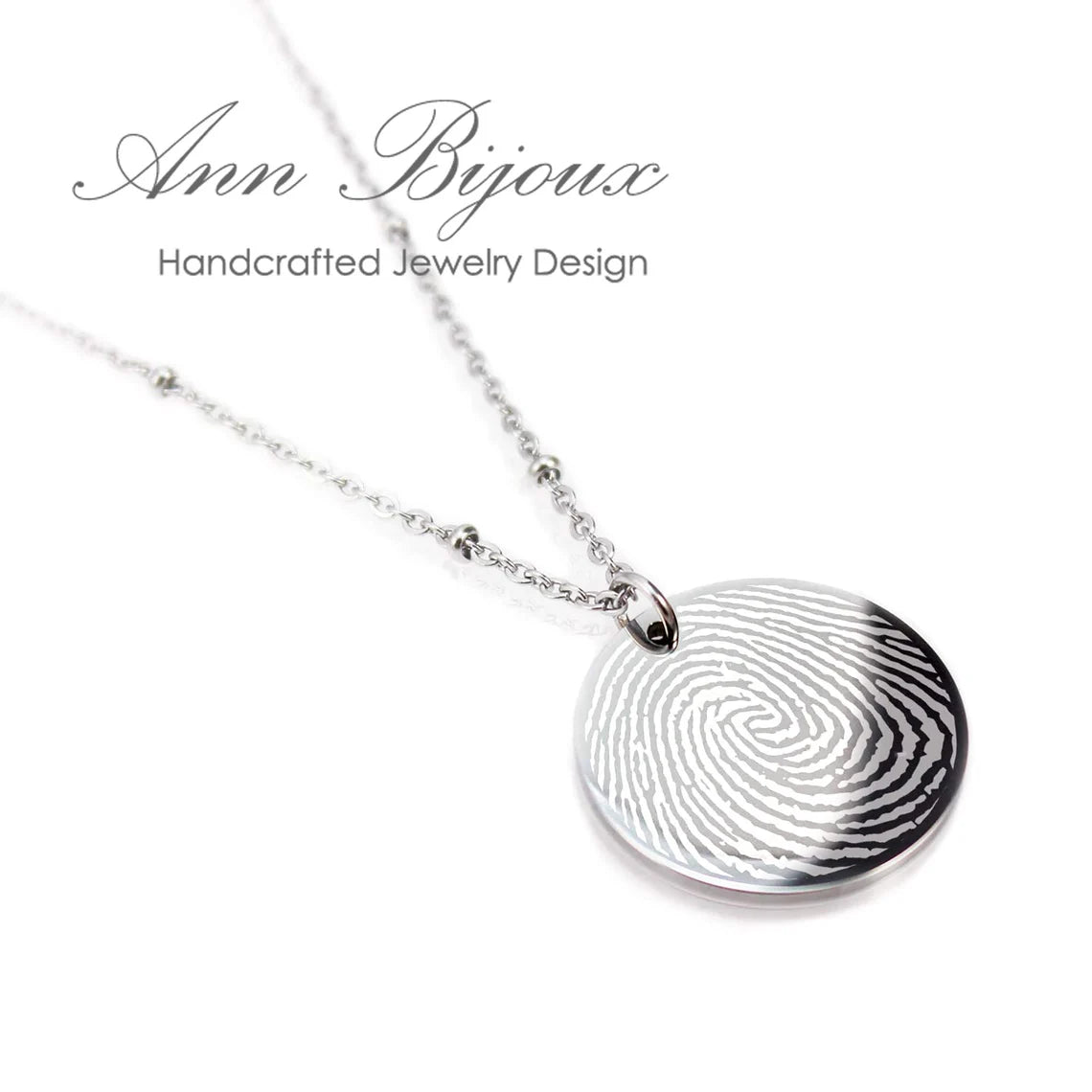 "Custom fingerprint jewelry: a polished circular silver pendant with an actual thumbprint engraving, paired with a trendy beaded satellite chain."