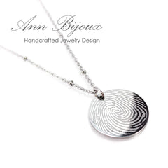 "Custom fingerprint jewelry: a polished circular silver pendant with an actual thumbprint engraving, paired with a trendy beaded satellite chain."