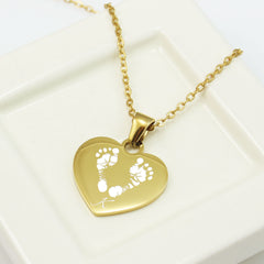 "A sentimental baby footprint heart necklace in silver, designed as a newborn keepsake or push present for moms. Features a custom name engraving alongside a pair of tiny footprints."