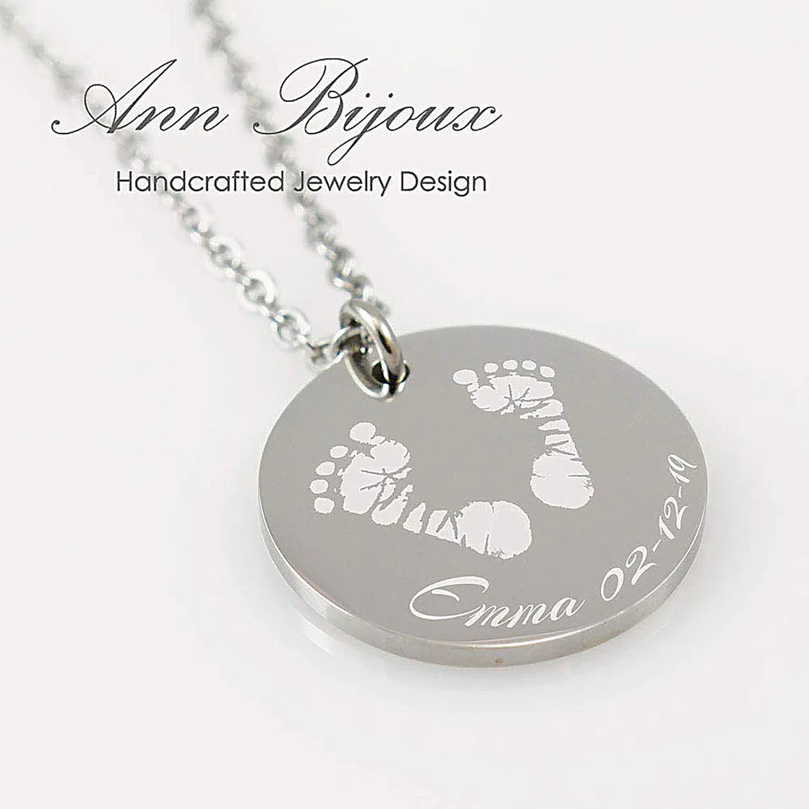 "Personalized infant footprint jewelry, showing a pair of engraved baby feet on a silver-tone circular pendant. A perfect newborn keepsake or memory necklace with custom date and name engraving."