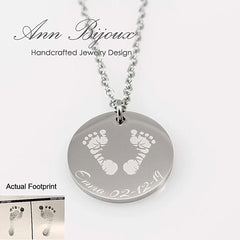 "Custom baby footprint necklace in silver. A highly detailed engraving of a newborn's actual footprints is etched onto a polished round disc pendant, personalized with the name 'Emma' and date '02.12.19'."