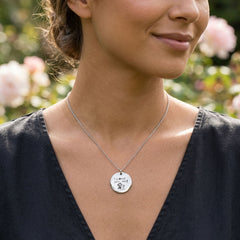 Woman wearing a necklace with a round pendant in a garden setting