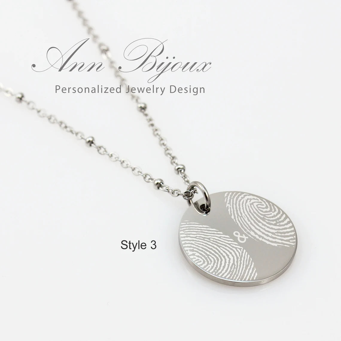 "Custom fingerprint jewelry: a polished circular silver pendant with an actual thumbprint engraving, paired with a trendy beaded satellite chain."