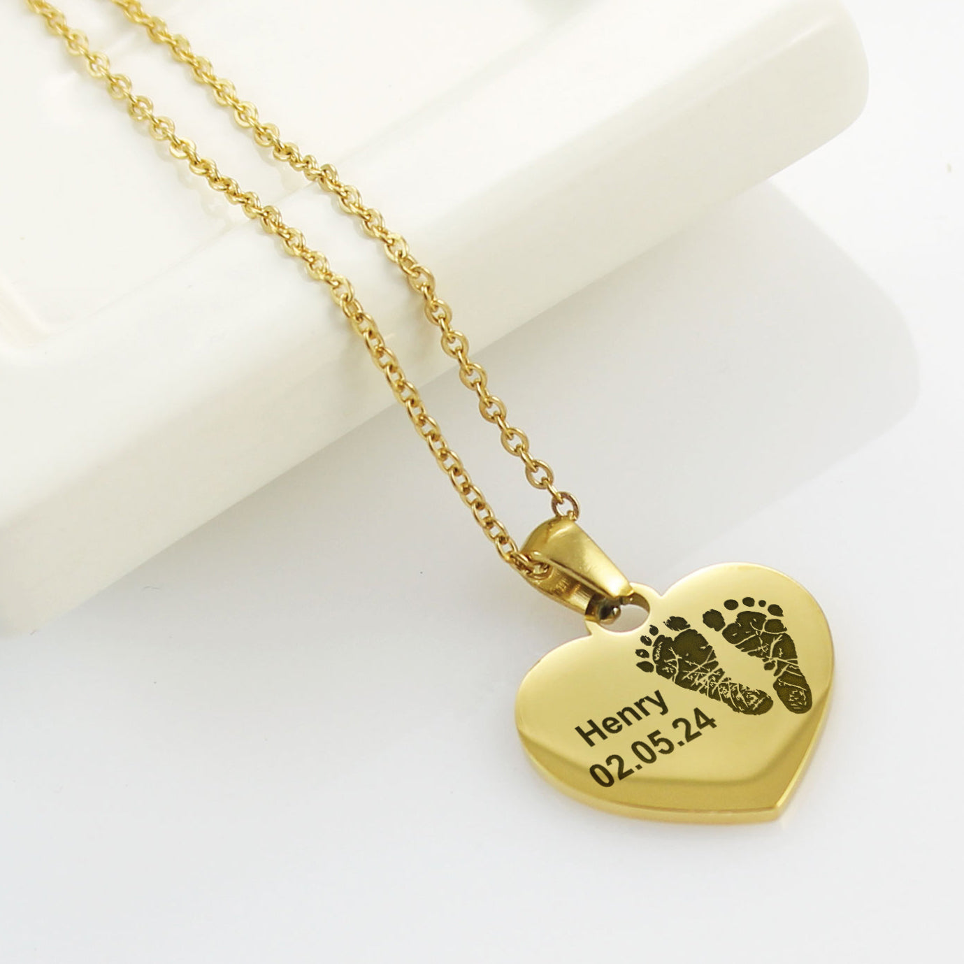 Gold heart-shaped necklace with engraved text and footprints on a white background