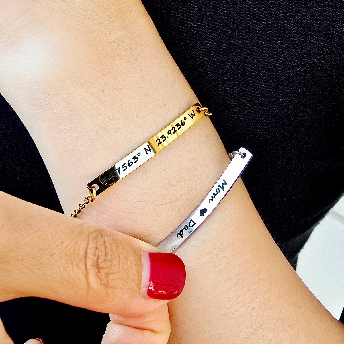 Two bracelets on a wrist with engraved text, one gold and one silver.