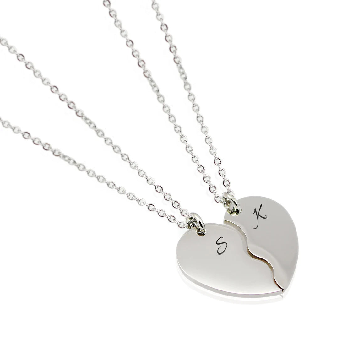 Two silver heart-half necklaces that fit together to form a full heart. Each piece is engraved with a single initial—'S' and 'K'—in a delicate black script font, hanging from matching cable chains.