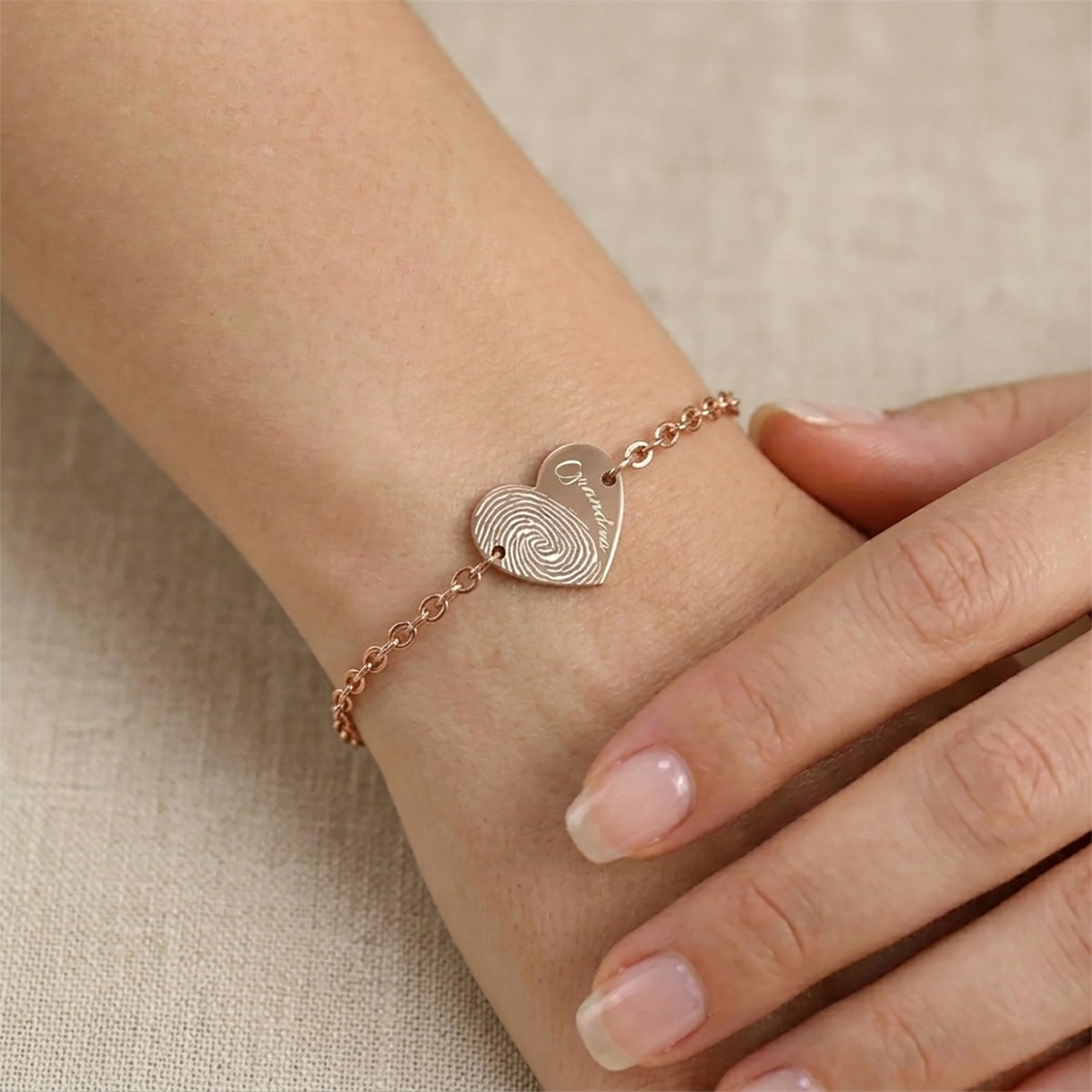 Rose gold bracelet with a heart-shaped charm on a wrist against a beige background