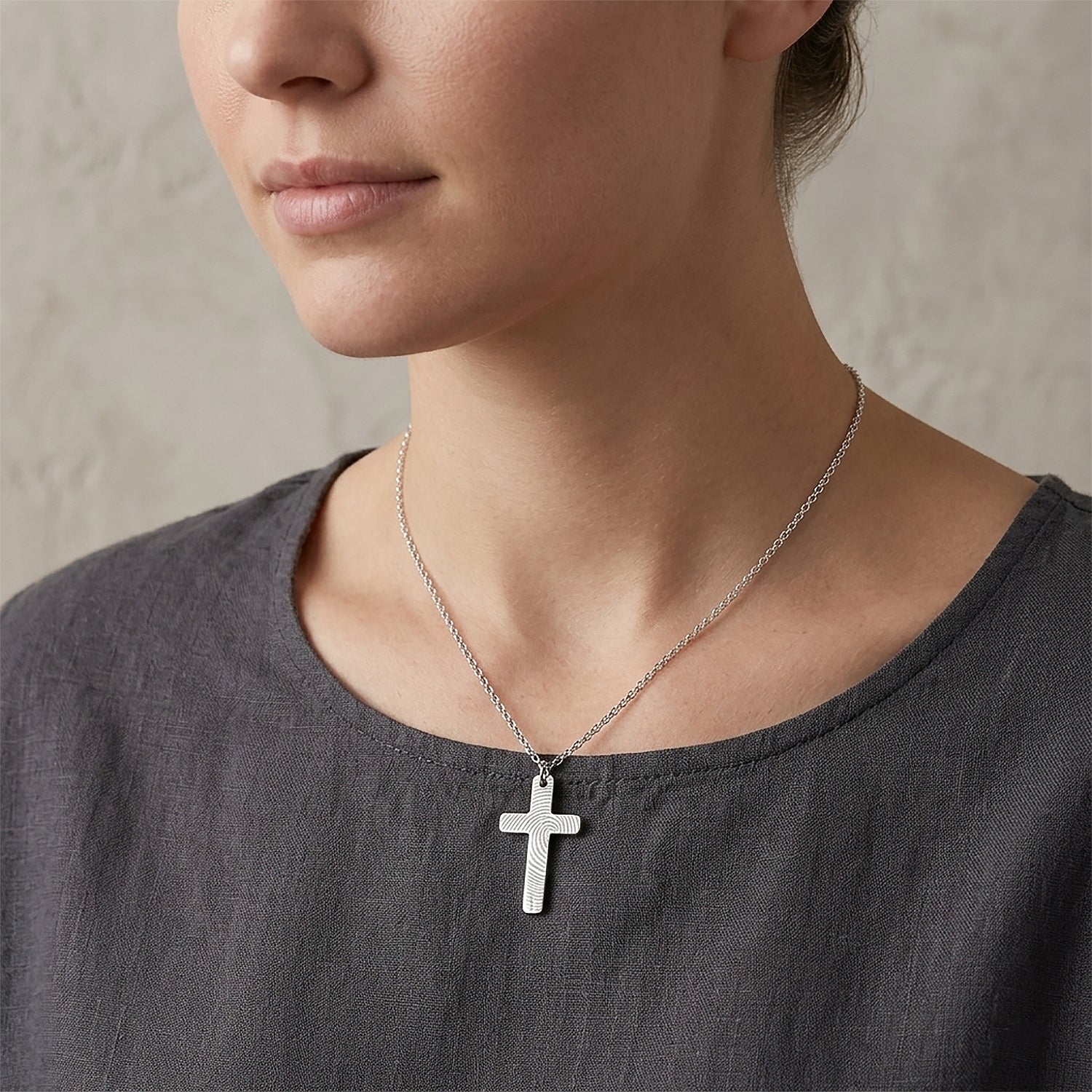 Person wearing a silver cross necklace against a neutral background