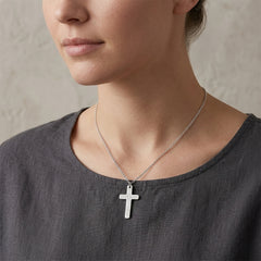 Person wearing a silver cross necklace against a neutral background