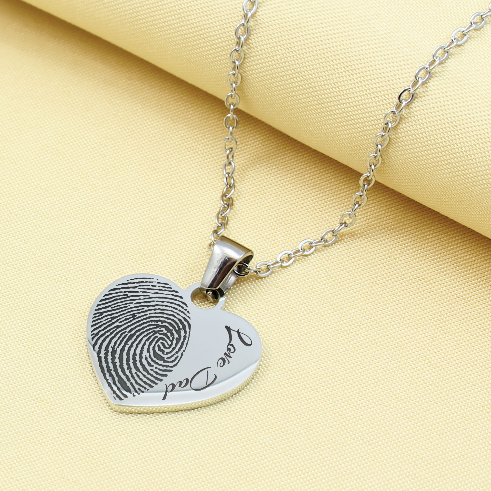 Heart-shaped fingerprint pendant necklace on a yellow fabric background