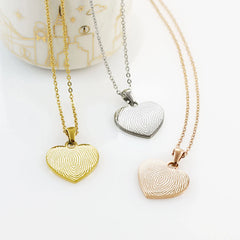 Three heart-shaped fingerprint necklaces in gold, silver, and rose gold finishes on matching cable chains.
